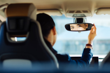 Skillful driver. Positive smart woman fixing the rearview mirror while looking into it