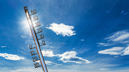 Hitzewelle-Hintergrund: Thermometer mit hohen Temperaturen, vor strahlender Sonne