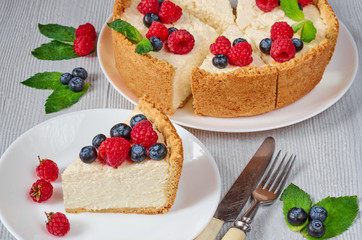 Slice of cheesecake with fresh berries on the white plate - healthy organic summer dessert. Classic New York cheesecake decorated with blueberries and raspberries on the blurred background. Side view