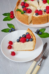Slice of cheesecake with fresh berries on the white plate close up - healthy organic dessert. Classic New York cheese cake decorated with blueberries and raspberries on the blurred background