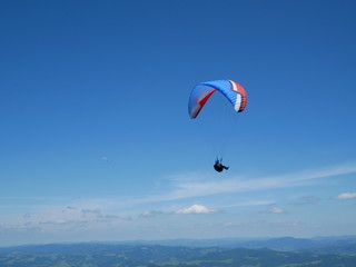 Carpathians / Ukraine - July 07 2017: Paraglider flying parachute in blue sky at a bright sunny summer day. Active lifestyle