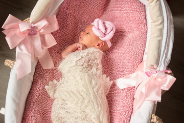 Fototapeta na wymiar Newborn baby girl comfortably lying in baby basket. Child wrapped in wool blanket.