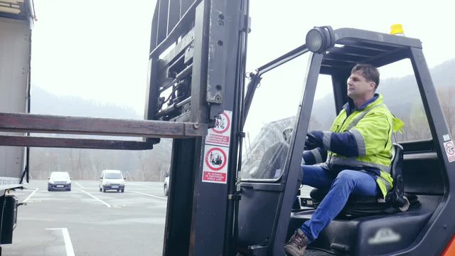 Professional forklift driver carefully picking cargo from trailer 4K. Medium shot of forklift driver in focus while operating the forks.