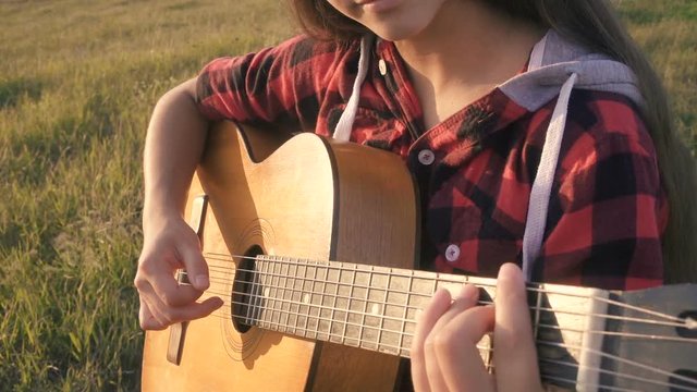 Young girl playing guitar on meadow at the sunset