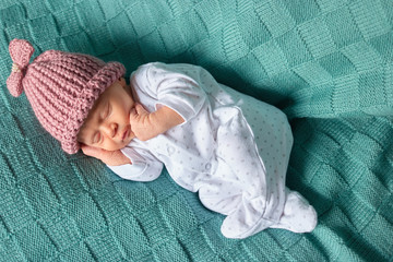 Sleeping baby girl with pink woolean hat. Newborn caucaisan baby sleeps deeply on green wool.