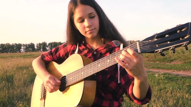 Young girl playing guitar on meadow at the sunset