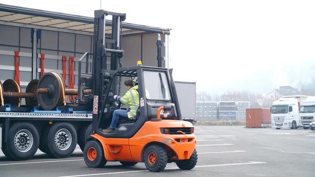 Industrial loading of cargo on big parking place 4K. Wide shot of forklift in focus unloading to trailer on the left side of the frame. Other trucks in the background on the right side.