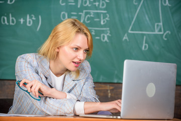 Organize class and make learning easy process. Present lesson in comprehensive manner use visual to facilitate learning. Teacher woman sit table work laptop surfing internet chalkboard background