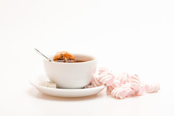 Tea mug with dipped teabag and marshmallows. Tea break concept. Process of drink brewing in cup. Mug filled with black brewed tea, spoon and heap of marshmallow on white background