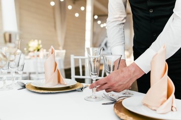 Waiter man serving Cutlery on tables in the restaurant to prepare for the reception of visitors