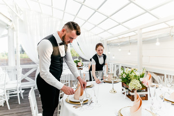 Two male and female waiters serve a table in the restaurant wiping glasses for wine
