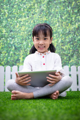 Asian Little Chinese girl sitting on the grass and playing with tablet