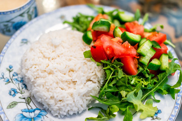 Macro closeup of plain white jasmine long grain cooked rice with arugula tomato salad on plate, table healthy vegan diet food
