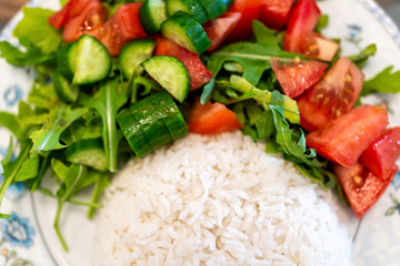Macro closeup flat top view down of plain white jasmine long grain cooked rice with arugula tomato salad on plate, table healthy vegan diet food