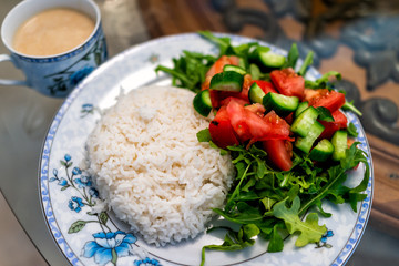 Macro closeup of plain white jasmine long grain cooked rice with arugula tomato salad on plate, cup with sauce or coffee drink, table healthy vegan diet food