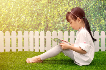 Asian Little Chinese girl sitting on the grass and playing with tablet