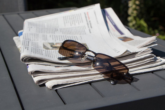Pile de journaux et lunettes de soleil sur une table de jardin