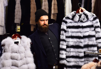 Guy with cunning face shows fur coats in fashion store.