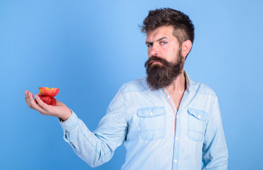Man strict face with beard offers organic treats.Hipster bearded holds strawberries and apple on palm. Man offers to try strawberries and apple fruit treats blue background. I have treats for you