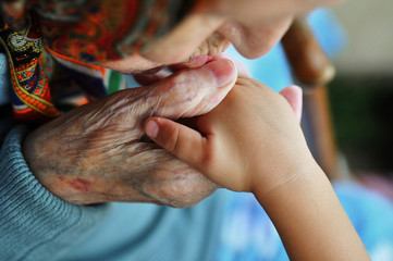 an elderly woman kissing children's hands. Summer walk on the street. 1 year and 90 years.