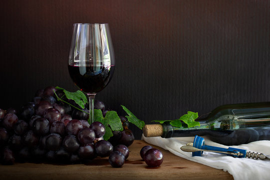 Glass of Wine with bunch of grape and wine bottle with wine opener on the wooden plank which has white cloth