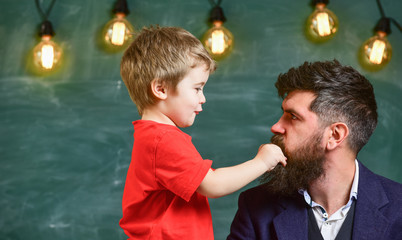 Teacher with beard, father and little son having fun in classroom, chalkboard on background. Dad...