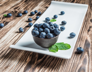 blueberry with mint on a white plate on a wooden background