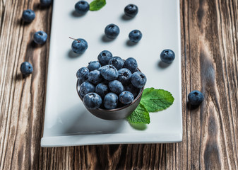 blueberry with mint on a white plate on a wooden background