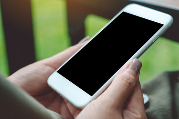 Mockup image of a woman holding white smart phone with blank black desktop screen with blur green nature background