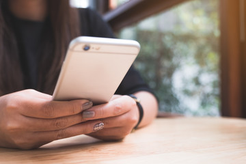 Closeup image of a woman holding , using and looking at smart phone with blur green nature background
