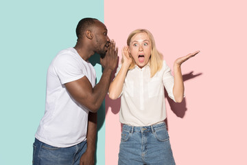 Fototapeta premium The young couple whispering a secret behind her hand over studio background