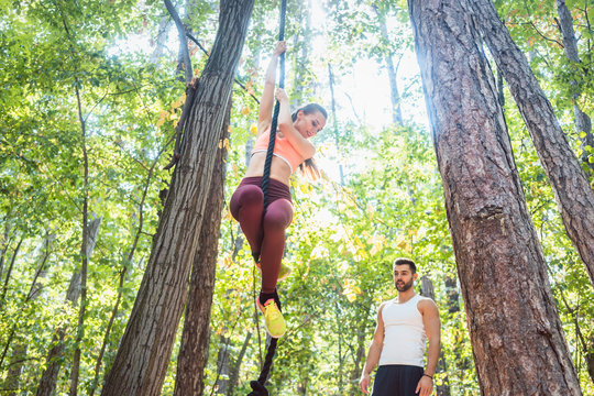 Woman climbing rope tied to a tree for better fitness in outdoor gym