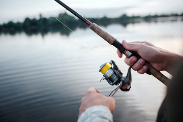 A picture of rotative spinner that guy holds in hands. He rotates reel with left hand. He is at...