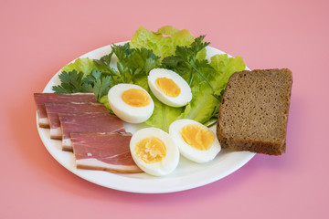 breakfast. Boiled eggs, bacon, greens in a white plate on pink background