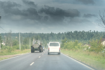 Traktor and white minivan on the rural road under the dark sky wth clouds