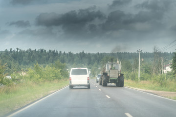 Fototapeta na wymiar Traktor and white minivan on the rural road under the dark sky wth clouds