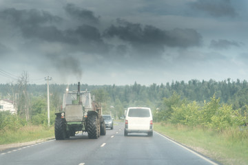 Traktor and white minivan on the rural road under the dark sky wth clouds