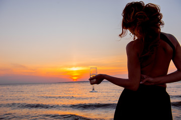 woman at sunset. Girl with glass on background setting sun. romantic date in the evening. girl on the beach.  woman  on the beach. Elegant girl is drinking champagne. hand with glass
