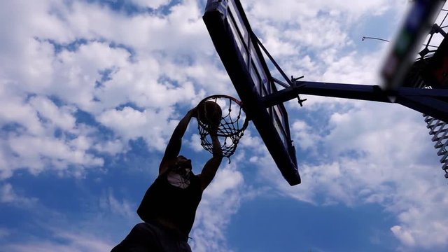 Street basketball. Performing slam dunk tricks. The player scores the ball in the basket. Slow-motion shooting of 240 frames per second