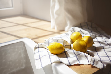 Close up shot of yellow lemons drying on checkered towel in rustic kitchen with sun shining through window. Picture of ripe citrus fruits lying on wooden counter by white sink. Selective focus - Powered by Adobe