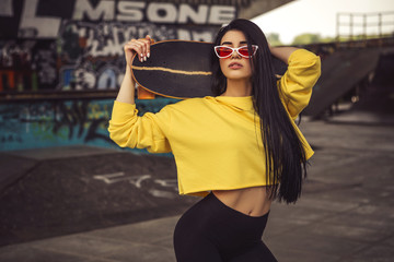 Sexy slim fit brunette woman in sport casual outfit in a skate park. Active leisure on a longboard
