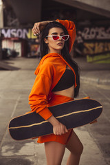 Sexy slim fit brunette woman in sport casual outfit in a skate park. Active leisure on a longboard