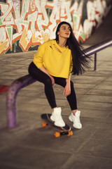 Sexy slim fit brunette woman in sport casual outfit in a skate park. Active leisure on a longboard