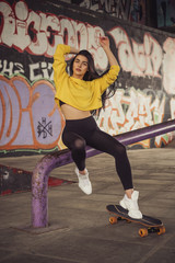 Sexy slim fit brunette woman in sport casual outfit in a skate park. Active leisure on a longboard
