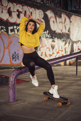 Sexy slim fit brunette woman in sport casual outfit in a skate park. Active leisure on a longboard