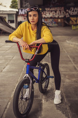 Sexy slim fit brunette woman in sport casual outfit in a skate park. Active leisure on a bicycle