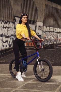 Sexy slim fit brunette woman in sport casual outfit in a skate park. Active leisure on a bicycle