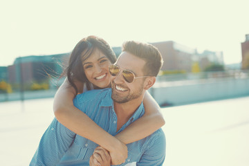 Happy young woman piggyback ride man outdoors in sunset