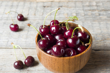 Juicy ripe cherries with twigs on wooden stand on rustic background.