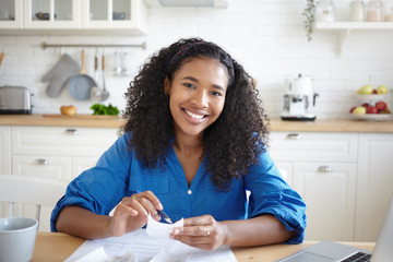 People, paperwork and modern technology concept. Picture of joyful young African woman holding pen...